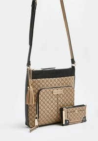 Borsa a tracolla e portafoglio coordinato in beige con motivo geometrico nero, dettagli dorati, tasca con zip frontale e pendaglio sulla borsa.