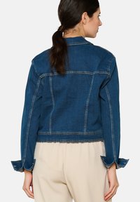 Tamsiai mėlyna prigludusi džinsinė striukė su trumpu dizainu. Yra dvigubai siuvinėtos siūlės, mygtukais prisispaudžiančios rankovės ir klasikinis apykaklė.