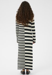 Pikk, sooneline kleit vertikaalsete mustade ja kreemjate triipudega. Kitsa lõikega varrukad, ümmargune kaelus ja maxipikkuse disain.