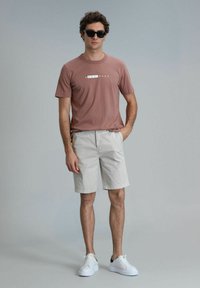 Casual outfit met een stofroze katoenen t-shirt met de tekst "HAPPINESS", beige shorts en witte sneakers met zwarte accenten.