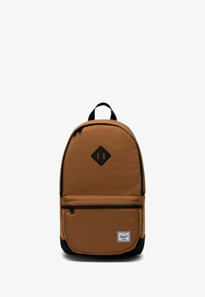 Sac à dos en tissu marron avec une base noire, un patch logo en forme de losange, une poche zippée à l'avant et une poignée supérieure pour le transport. Détail de fermeture éclair sur le compartiment principal.