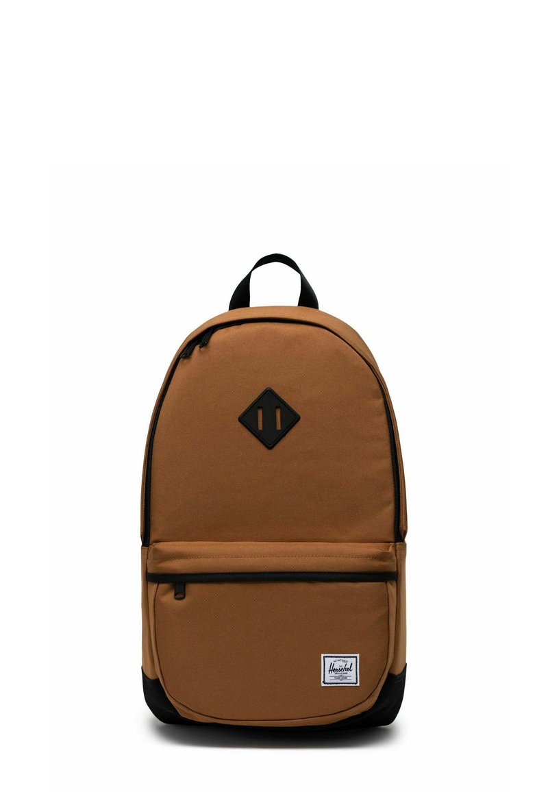 Sac à dos en tissu marron avec une base noire, un patch logo en forme de losange, une poche zippée à l'avant et une poignée supérieure pour le transport. Détail de fermeture éclair sur le compartiment principal.