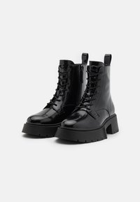 Zwarte enkellaarsjes van lakleer met een stevige hak, veters aan de voorkant, een zijrits en een lus aan de achterkant voor gemakkelijk aan- en uittrekken.