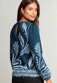 Blusa de un oscuro tono verde azulado con estampados botánicos en blanco, mangas abullonadas, un escote tipo keyhole en la espalda y puños elásticos. Tejido suave con un dobladillo estampado.