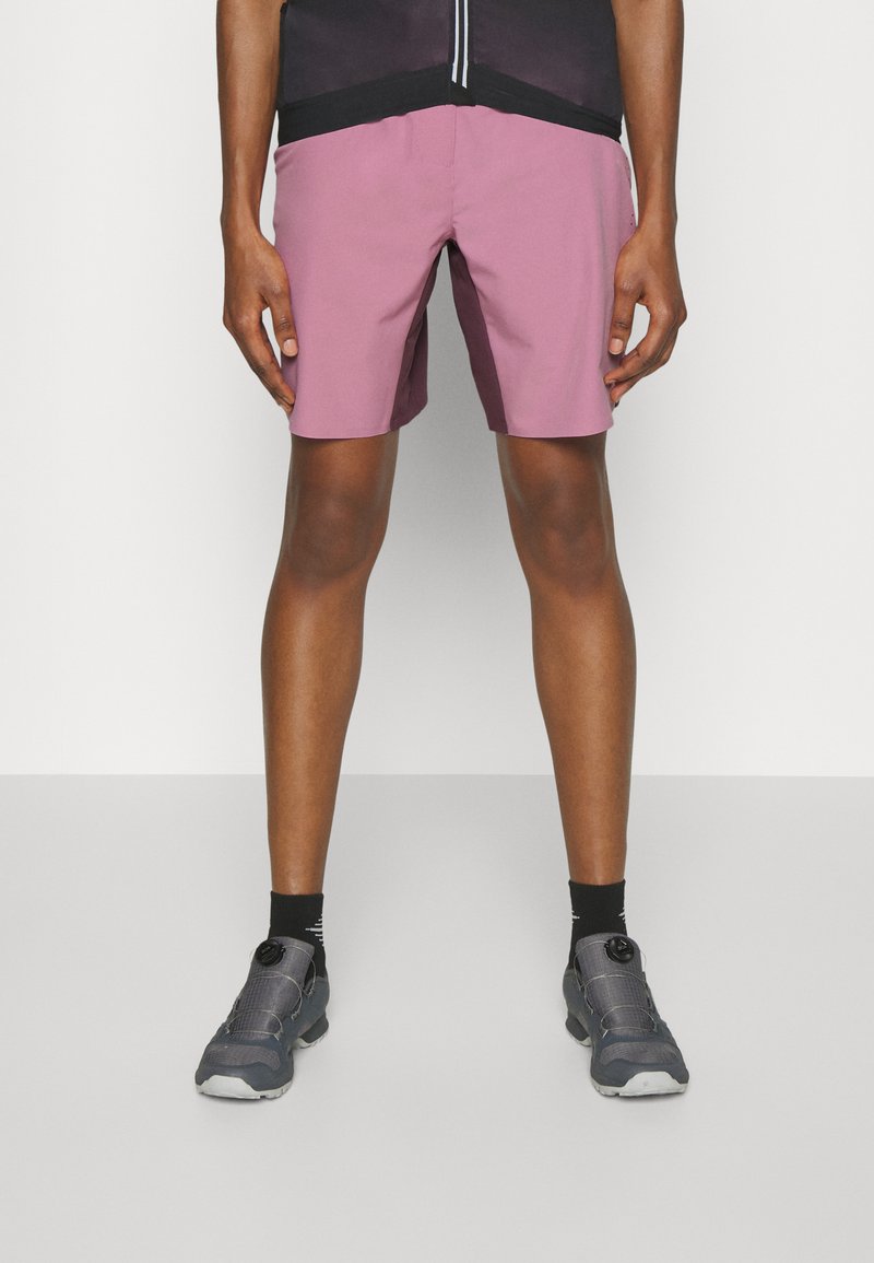 Lichte roze shorts met een ontspannen pasvorm en een elastische tailleband. Gecombineerd met grijze sneakers en zwarte enkelsokken.