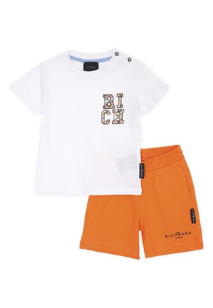 T-shirt bianca in cotone con grafica colorata "RICH" e due bottoni a pressione neri sulla spalla, abbinata a pantaloni corti arancioni con vita elastica.