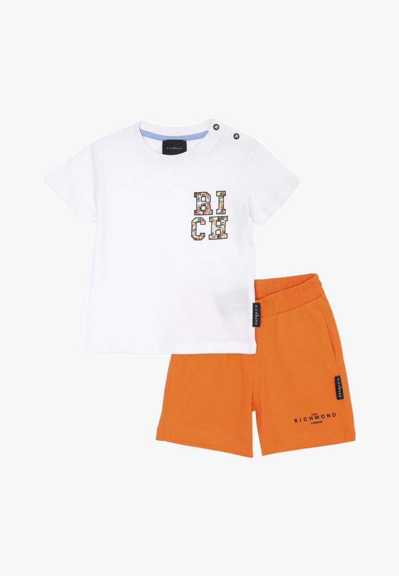T-shirt bianca in cotone con grafica colorata "RICH" e due bottoni a pressione neri sulla spalla, abbinata a pantaloni corti arancioni con vita elastica.
