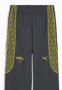 Pantalon de sport gris foncé avec des bandes latérales géométriques jaunes, logo Pokémon et Poké Ball sur la jambe gauche, et logo Puma jaune sur la jambe droite.