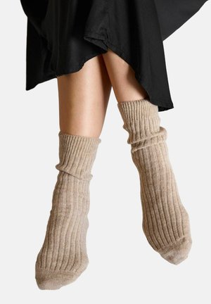 Beige geribbelde sokken met een zachte textuur, met een losse pasvorm, net boven de enkel, gecombineerd met een zwarte rok.