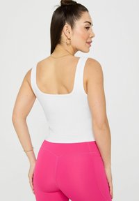 White ribbed tank top with wide straps, paired with bright pink leggings. Smooth texture, fitted design, showcasing a sleek silhouette.