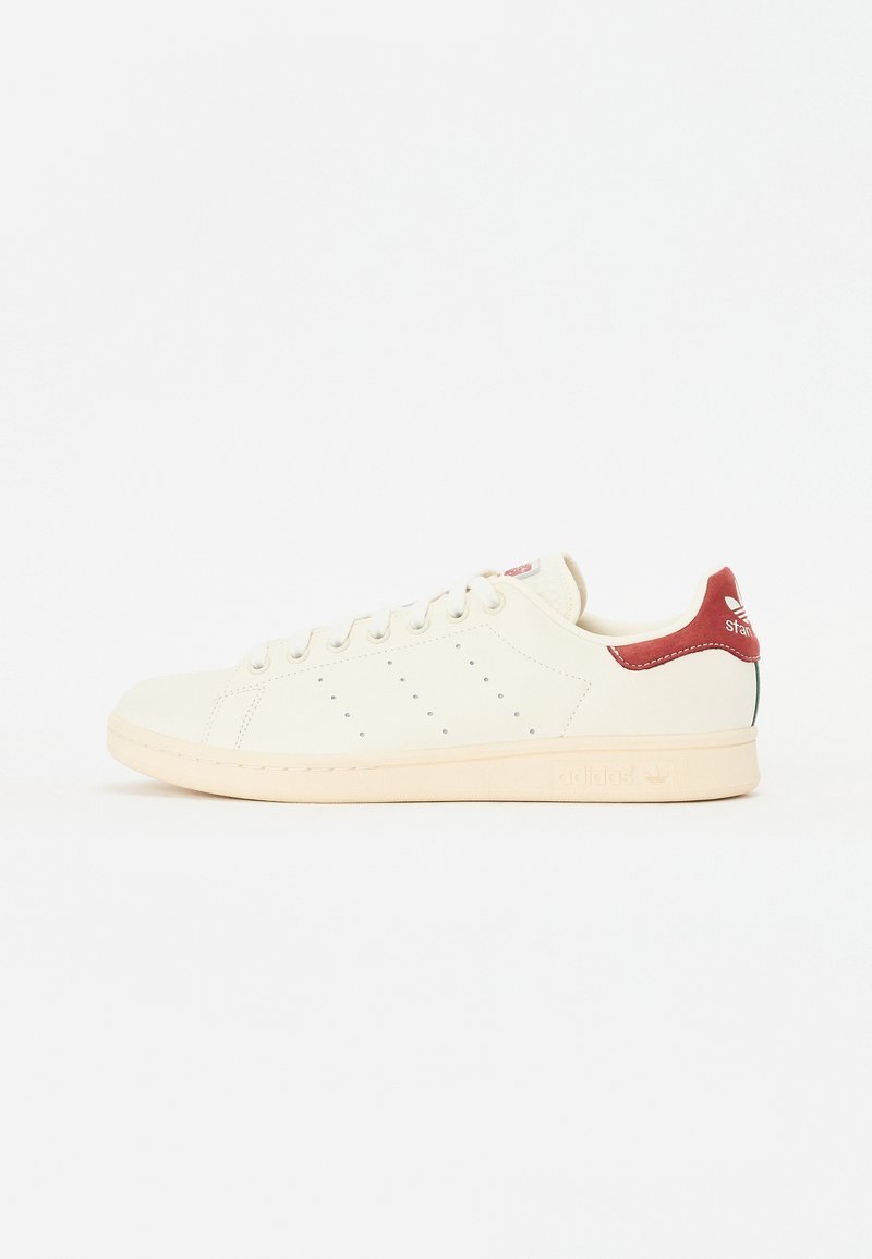 Biele kožené tenisky s perforovaným dizajnom, krémovou gumovou podrážkou, červeným pätkovým prvkom a zeleným akcentom. Obsahujú klasické šnurovanie.