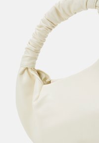 Bolso de mano en crema con una forma suavemente estructurada, asa de cuero sintético fruncido y un acabado suave y mate.