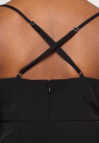 Black dress with crossed spaghetti straps, featuring a textured fabric and a discreet zipper detail at the back.