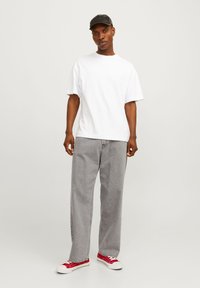 Maglietta bianca in cotone, vestibilità comoda; pantaloni in denim grigi, gamba dritta; sneakers rosse con suola bianca; cappellino nero. Design minimalista, senza motivi.