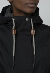 Black jacket with a hood, featuring gray and brown drawstrings, silver hardware, and a smooth fabric texture. No visible patterns or accents.