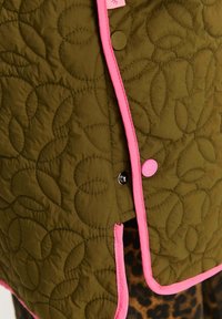Olivovo zelená prešívaná bunda s textúrou listového vzoru, lemovaná ružovou, s patentným zapínaním a kontrastnými detailmi.
