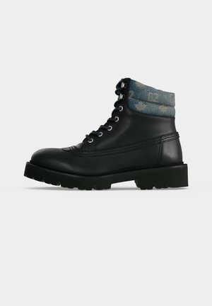 Botte en cuir noir à lacets avec une semelle épaisse et un col en denim rembourré présentant des motifs bleu clair, vue de côté extérieur.