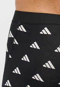 Μαύρο ύφασμα μποξερ σορτς με επαναλαμβανόμενο λευκό τριγωνικό σχέδιο και μαύρη ελαστική μέση. Ιδανικό για άνεση και εφαρμογή.