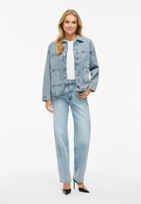 Helle blaue Jeansjacke mit Knopfverschluss, aufgesetzten Taschen und langen Ärmeln, kombiniert mit passenden hellblauen Jeans und schwarzen Absatzschuhen.