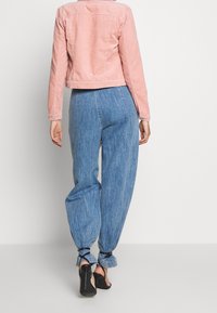 Lyserød corduroyjakke med en cropped design, parret med løse blå denimjeans med ankelbindinger. Sorte højhælede sko fuldender outfittet.