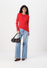 Rød langermet topp med ribbontrekk på ermene, kombinert med lyseblå vide jeans og en svart håndveske. Firkantede brune hæler.