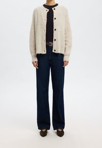 Beige stickad cardigan med rund halsringning, knäppning med knappar och ribbade ärmslut, tillsammans med mörkblå vida jeans och brun bälte.