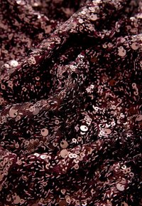Gros plan sur un tissu foncé densément couvert de petites paillettes brillantes couleur or rose créant des plis texturés et scintillants.