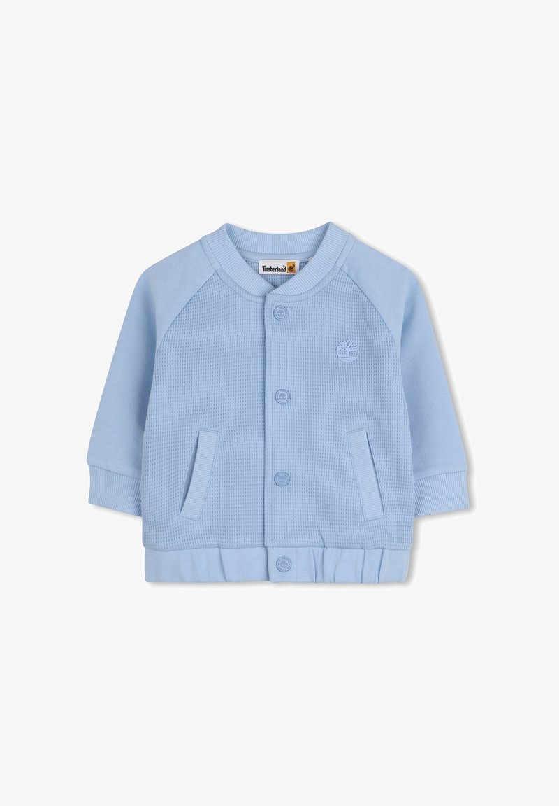 Veste boutonnée bleu clair avec un corps texturé, des manches unies, des poignets et un ourlet côtelés. Comprend deux poches avant et un logo en accent.