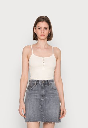 Witte geribde cami-top met dunne bandjes en knoopdetails aan de voorkant, gecombineerd met een grijze denimrok met een rafelige zoom en zakken.