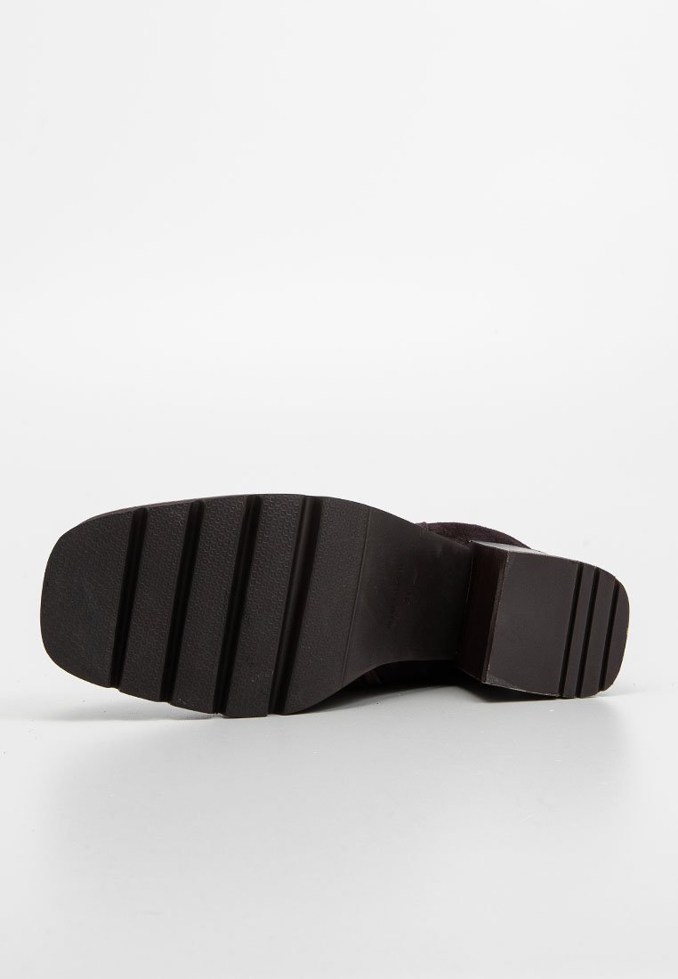 Czarna podeszwa buta z teksturowanej gumy, z poziomymi rowkami i projektowanym na pięcie w stylu warstwowym. Czysta i solidna struktura.