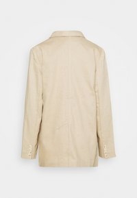Blazer beige à manches longues avec col et poignets boutonnés, vu de dos sur un fond blanc uni.
