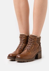 Bottines en cuir marron avec une finition texturée, un laçage à l'avant, un col en fourrure et un talon épais avec une semelle crantée.