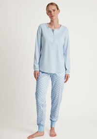 Lichtblauw langemouw shirt met knoopsluiting; lichtblauwe pyjamabroek met polkadots en cuffs bij de enkels. Zachte stof, casual pasvorm.