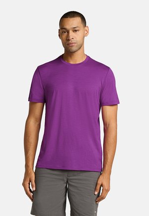 T-shirt violet à manches courtes en tissu lisse et léger, avec un col rond. Coupe décontractée et design minimaliste, associé à un short gris.