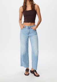 Černý zkrácený top bez rukávů, světle modré široké džíny s obroušeným lemem, doplněné tmavě hnědými plochými sandály. Hladký materiál a volný střih.