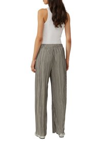 Lichtgrijze, geplooide broek met wijde pijpen en een elastische tailleband, gecombineerd met een witte tanktop, gezien van achteren.