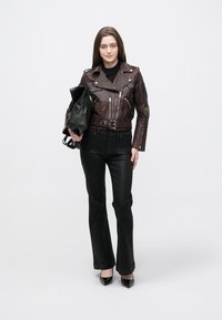 Bordó bőrdzseki szegecsekkel és foltokkal, fekete bővülő nadrággal és hegyes fekete magassarkúval párosítva, fekete táskát tartva.