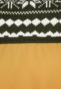 Stickad tyg i mörkgrön med vita geometriska mönster upptill; nedan, ett slätt, strukturerat senapsgult material.