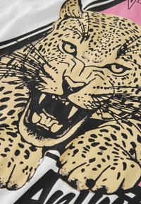 Valkoinen t-paita, jossa on suuri musta ja kultainen leopardigrafiikka, jossa on näkyvät hampaat, näkyvät pilkut ja rohkeat ääriviivat.