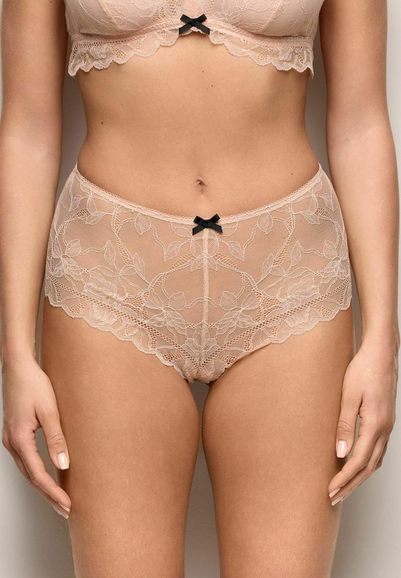 Beige kanten bh en hoogtallige kanten slipset met kleine zwarte strikjes op het midden van de bh en de tailleband van de slip.