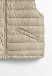 Beżowa pikowana kamizelka z przednim zamkiem błyskawicznym i boczną kieszenią. Materiał wydaje się gładki, lekko połyskujący i lekki w strukturze.