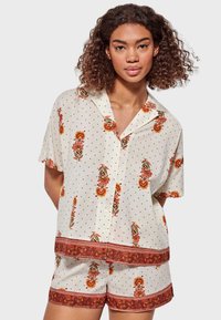 Conjunto de pijama de manga corta en color crema con lunares negros, estampados florales en naranja y verde, y ribetes estampados en los pantalones cortos y la parte superior.