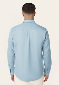 Lichtblauw overhemd met lange mouwen, voorzien van een button-down kraag, ribbeltextuur, afgeronde zoom en knopenmanchetten. De achterkant heeft een middenplooidetail.