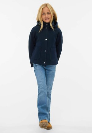 Marine fleecejakke med hætte, trykknaplukning og to forlommer; parret med lyseblå flared jeans og brune støvler.