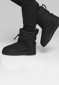 Bottes isolées noires avec un dessus en tissu texturé, lacets et semelle en caoutchouc plate. Présente un col rembourré et un détail de logo.