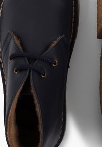 Scarpe di pelle blu navy con fodera in pelliccia marrone, dotate di lacci scuri e occhielli in tonalità oro. I dettagli delle cuciture lungo la suola esaltano il design.