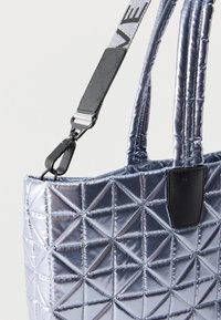 Μεταλλική ασημένια τσάντα tote με γεωμετρικό κεντητό σχέδιο, διπλές λαβές και αφαιρούμενο ρυθμιζόμενο λουρί ώμου με ασπρόμαυρη επωνυμία.