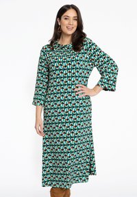 Langes, A-Linien Kleid aus einem gemusterten Stoff mit türkisfarbenen, weißen, braunen und schwarzen geometrischen Formen. Dreiviertelärmeln, runder Ausschnitt.