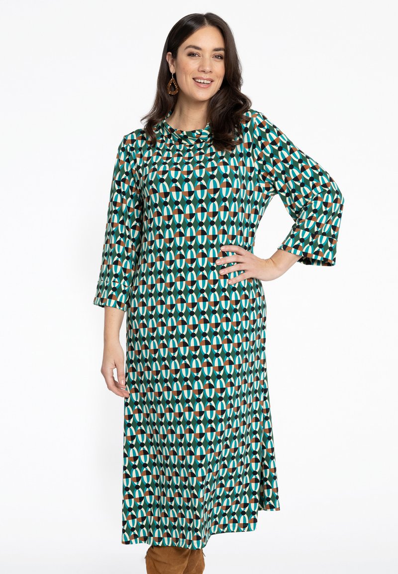 Langes, A-Linien Kleid aus einem gemusterten Stoff mit türkisfarbenen, weißen, braunen und schwarzen geometrischen Formen. Dreiviertelärmeln, runder Ausschnitt.