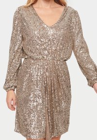 Paljetklänning i metallisk guld, med V-ringning, långa ärmar och elastisk midja för en avslappnad passform. Slät textur, glänsande yta.
